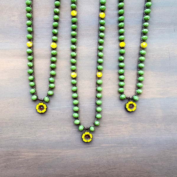 Three green beaded necklaces with yellow flower pendants on a wooden surface