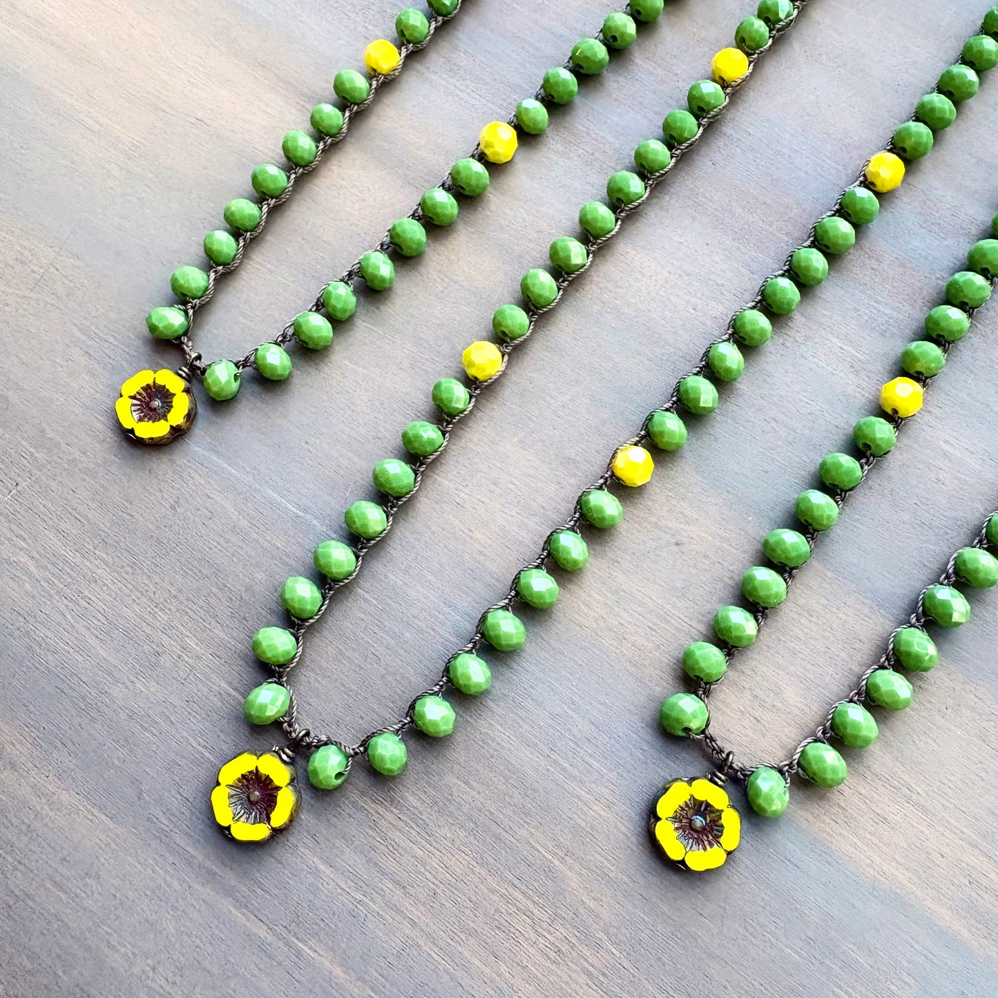 Green beaded necklace with yellow flower pendants on a wooden surface