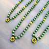 Green beaded necklace with yellow flower pendants on a wooden surface