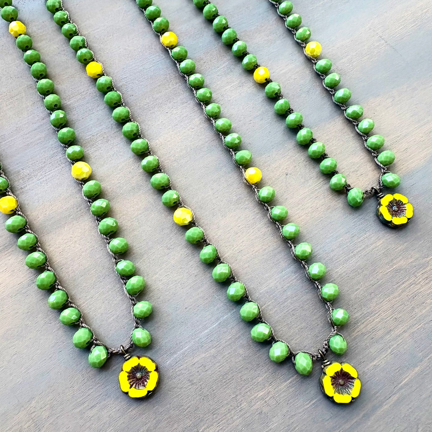 Green beaded necklaces with yellow flower pendants on a wooden surface