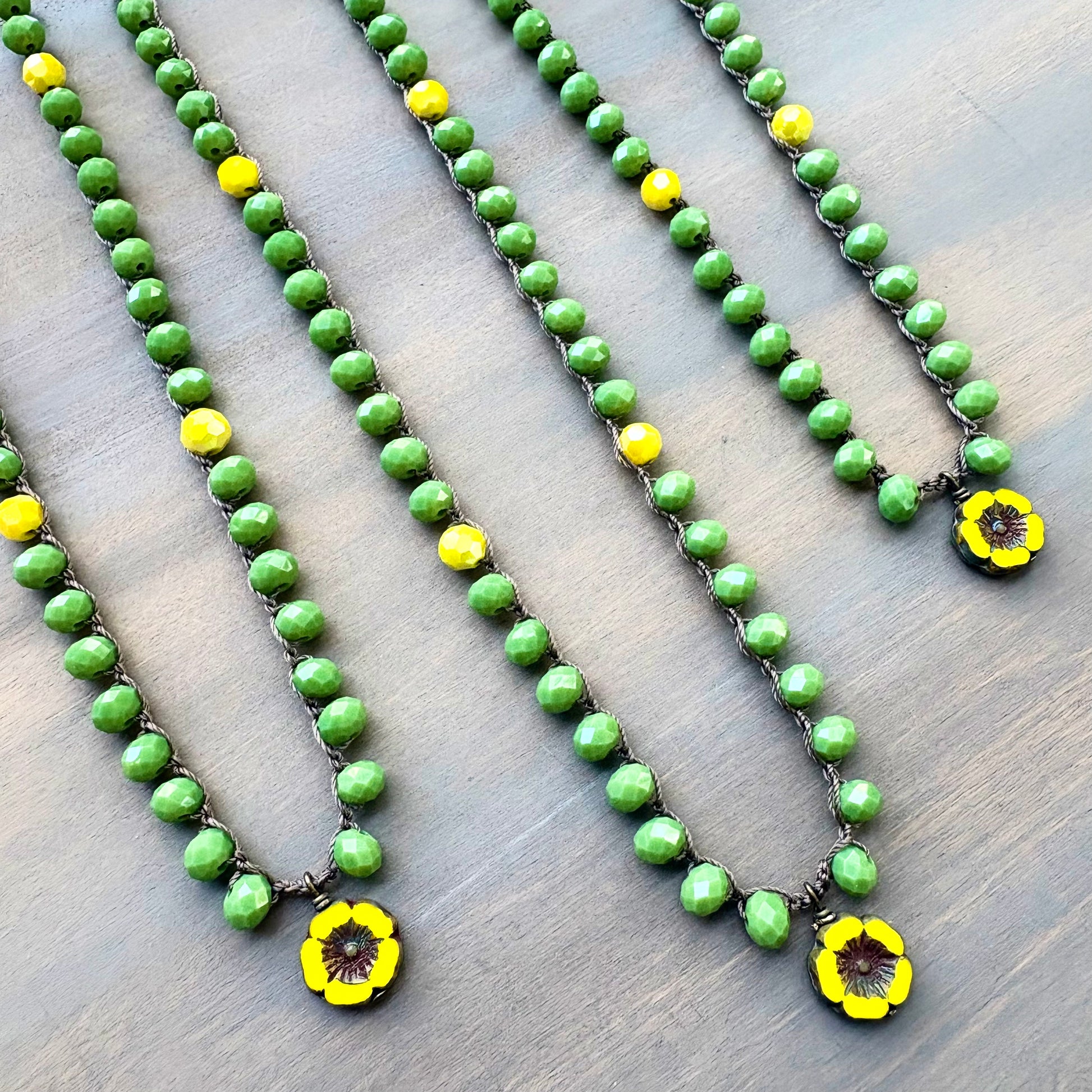 Green beaded necklaces with yellow flower pendants on a wooden surface