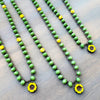 Green beaded necklaces with yellow flower pendants on a wooden surface