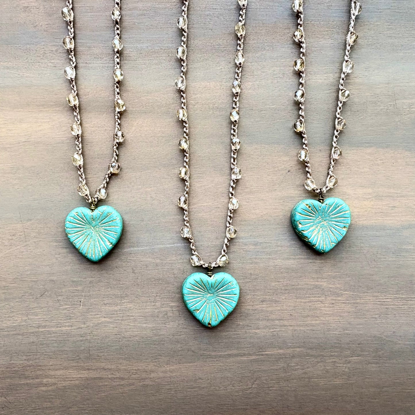 Two turquoise heart-shaped pendants on silver chains against a wooden background