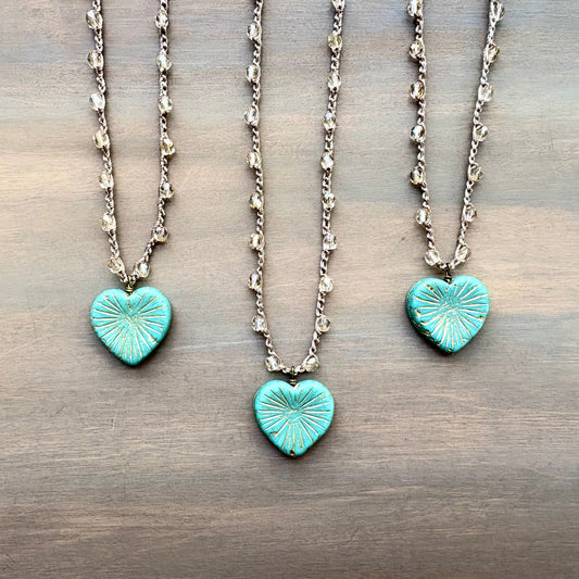 Two turquoise heart-shaped pendants on silver chains against a wooden background