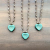 Two turquoise heart-shaped pendants on silver chains against a wooden background