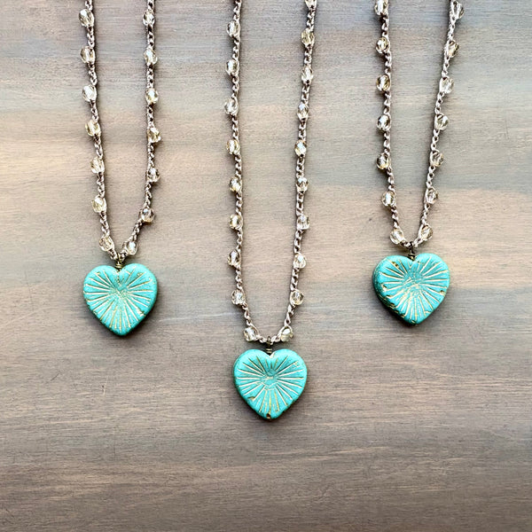 Two turquoise heart-shaped pendants on silver chains against a wooden background