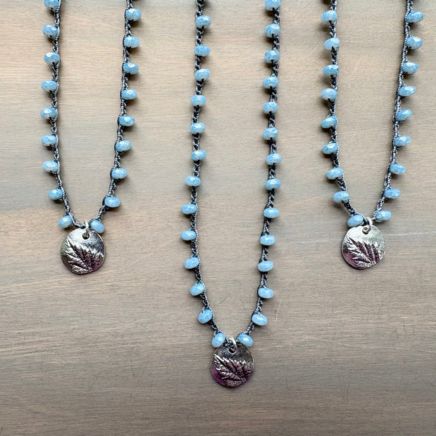 Three necklaces with blue beads and leaf-shaped pendants on a wooden surface