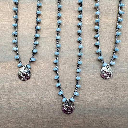 Three necklaces with blue beads and leaf-shaped pendants on a wooden surface