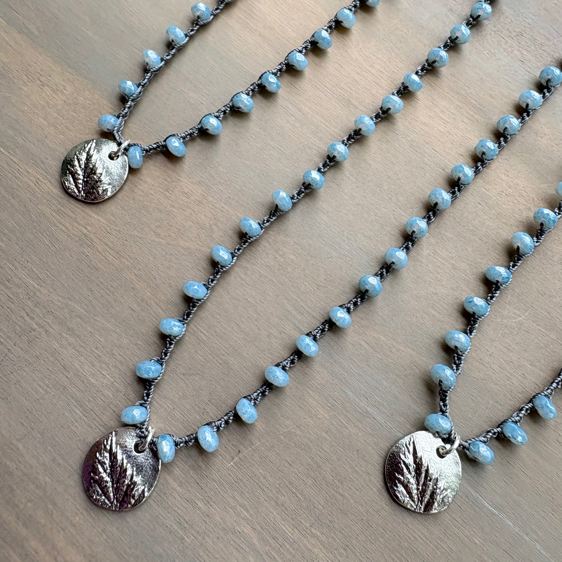 Necklace with blue beads and silver leaf pendants on a wooden surface