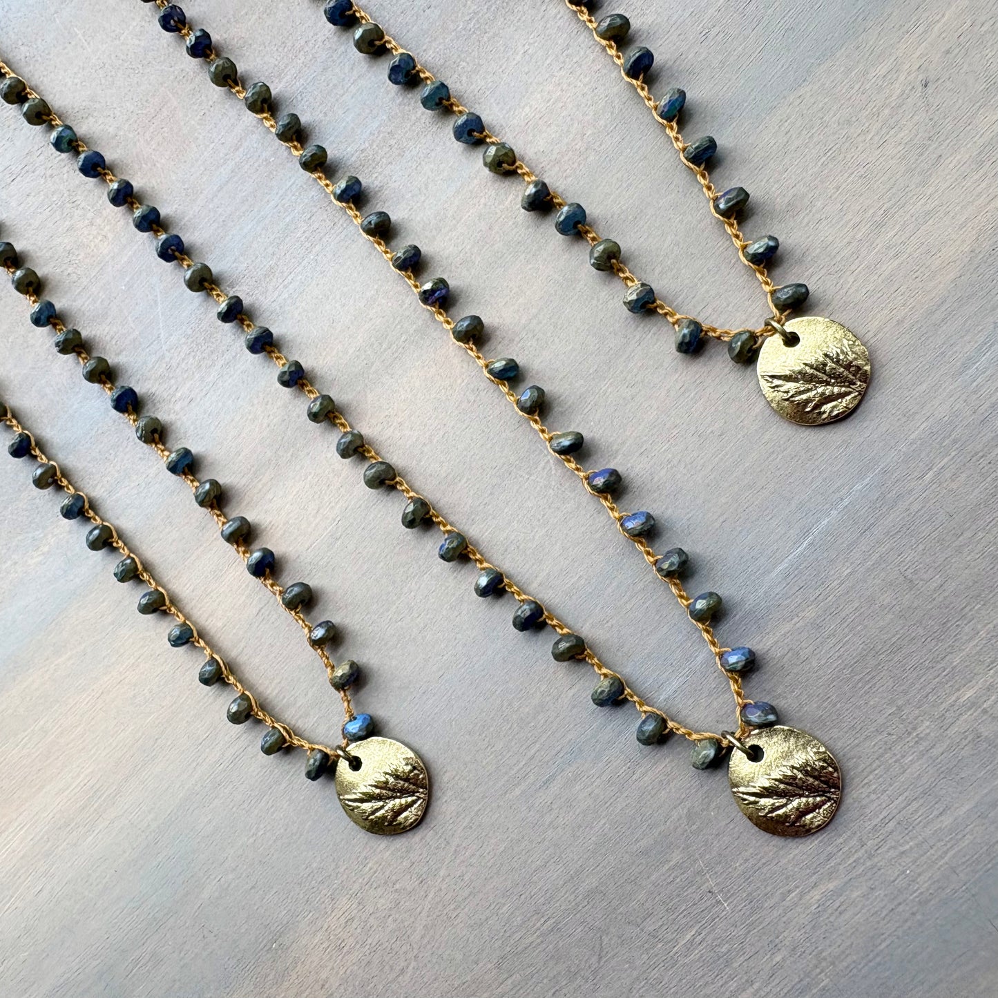 Two beaded necklaces with gold pendants on a light wooden surface