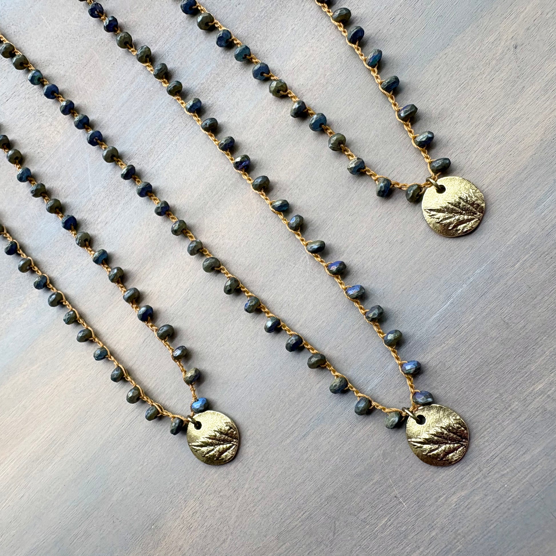 Two beaded necklaces with gold pendants on a light wooden surface