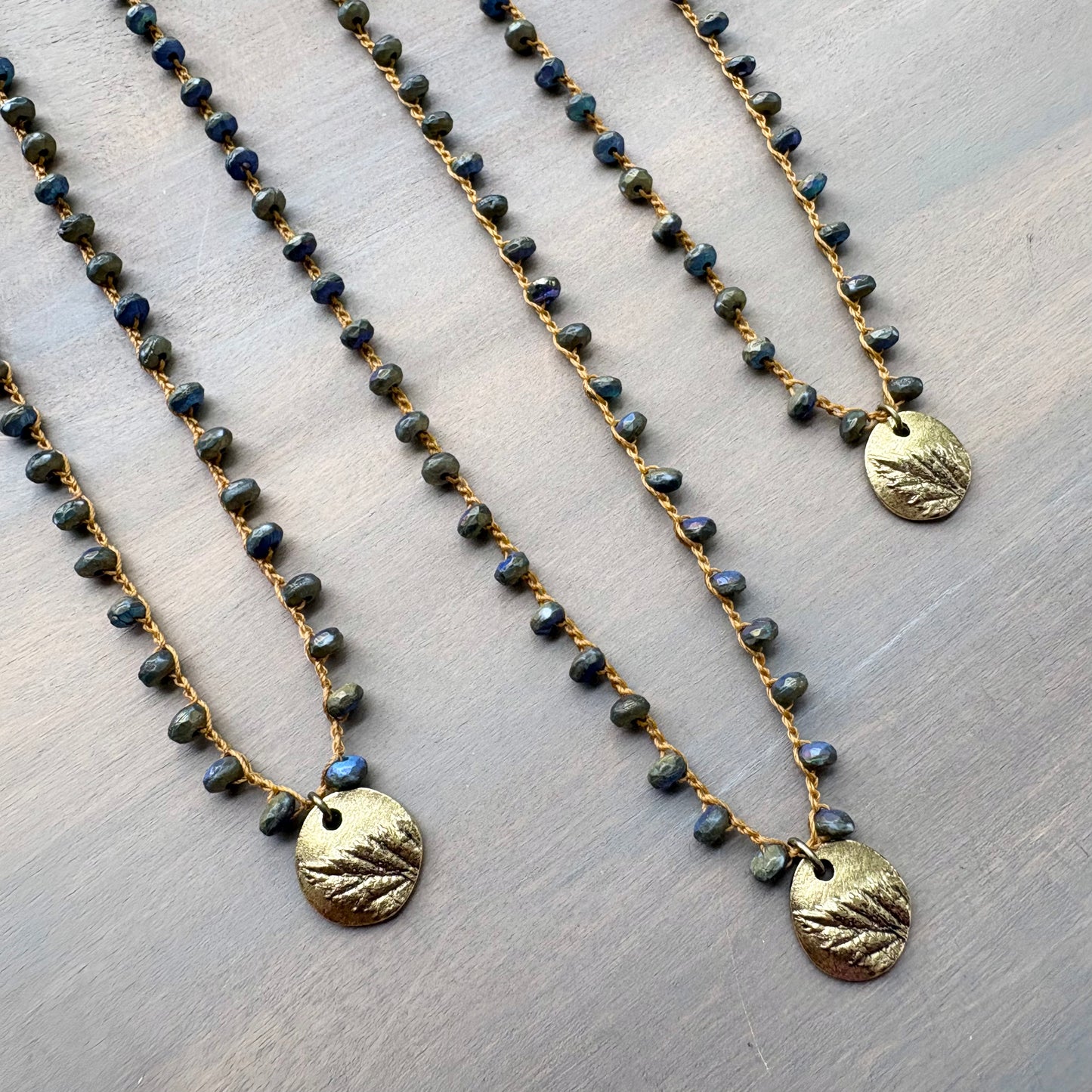 Two beaded necklaces with gold pendants on a textured surface