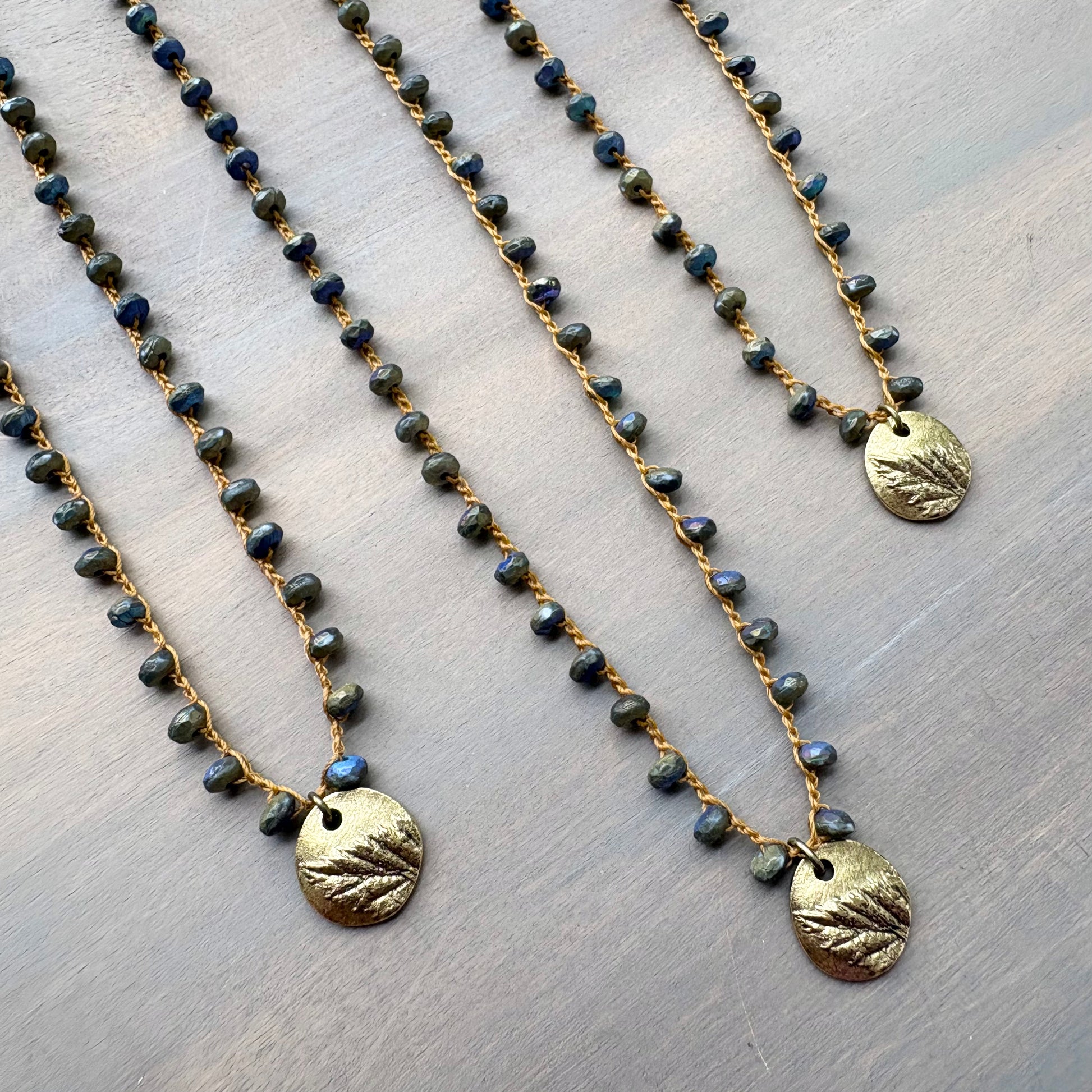 Two beaded necklaces with gold pendants on a textured surface