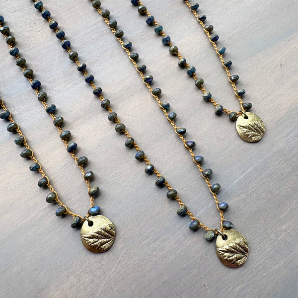 Two beaded necklaces with gold pendants on a textured surface