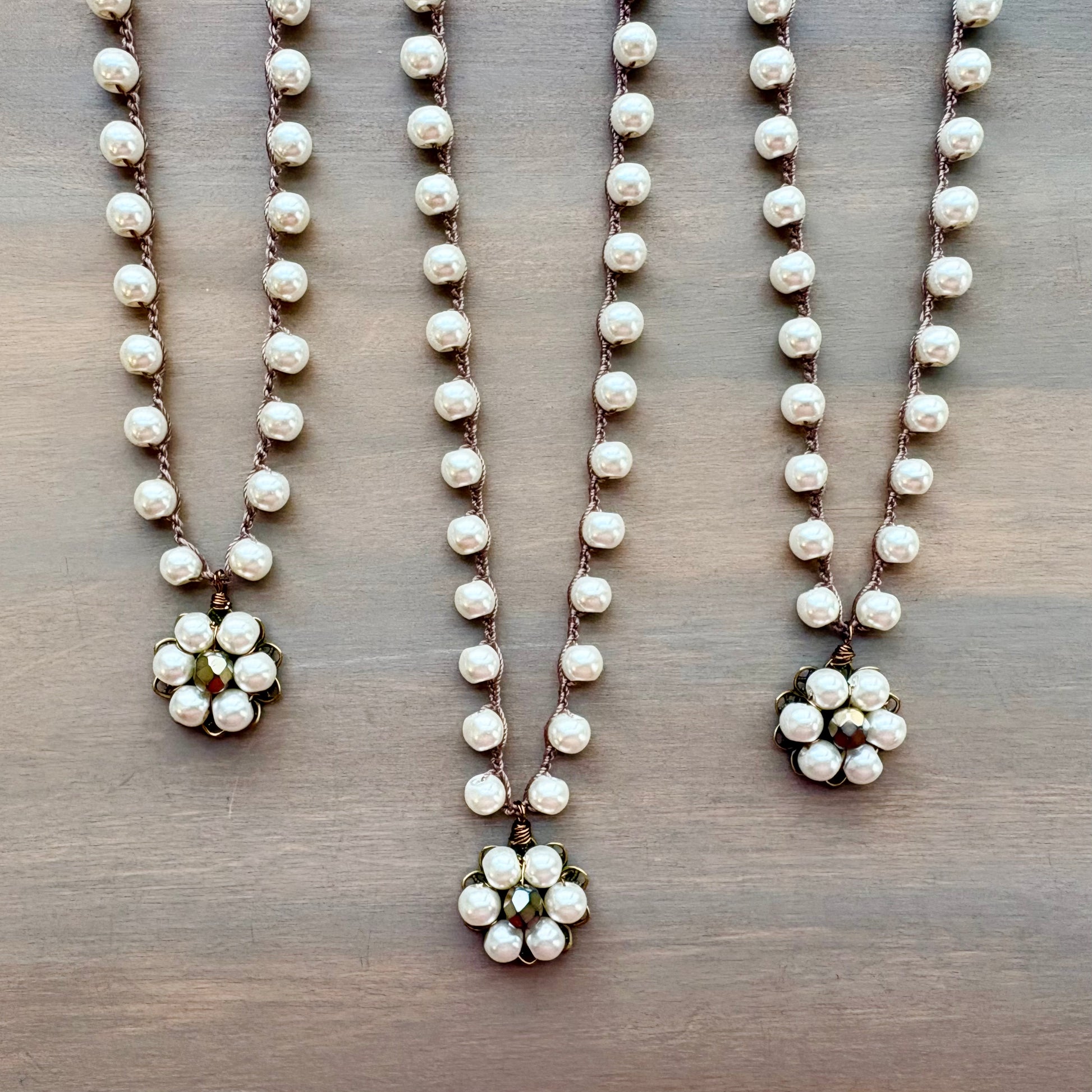 Three pearl necklaces with floral pendants on a wooden surface