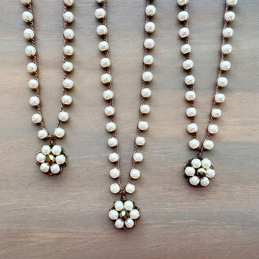 Three pearl necklaces with floral pendants on a wooden surface