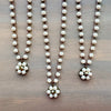 Three pearl necklaces with floral pendants on a wooden surface