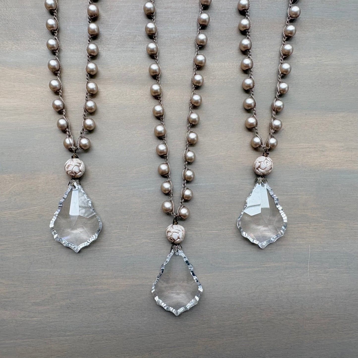 Two pearl necklaces with teardrop pendants on a wooden surface