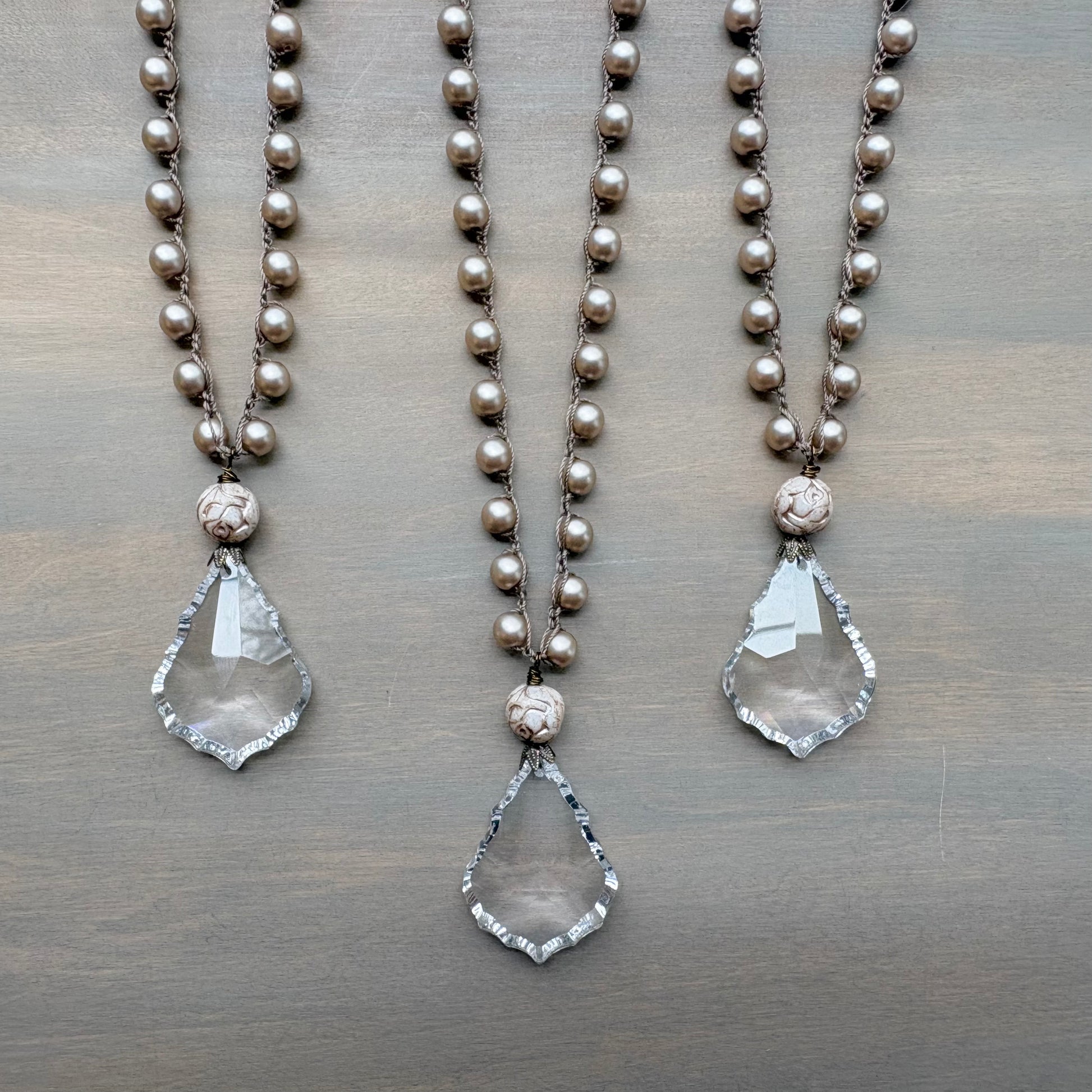 Two pearl necklaces with teardrop pendants on a wooden surface