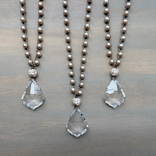 Two pearl necklaces with teardrop pendants on a wooden surface
