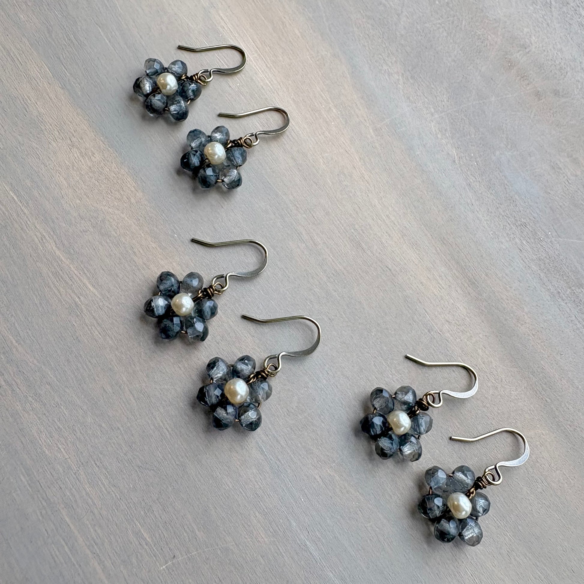 Set of flower-shaped earrings with blue and pearl beads on a wooden surface