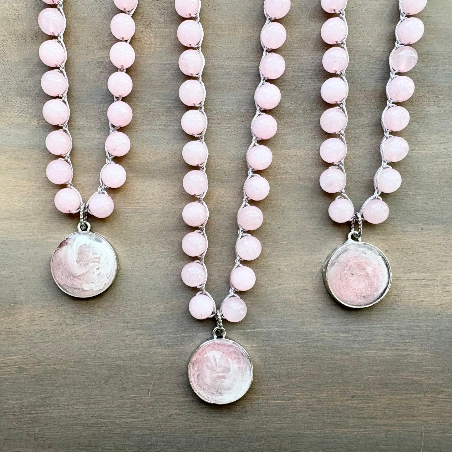 Three pink beaded necklaces with silver pendants on a wooden surface