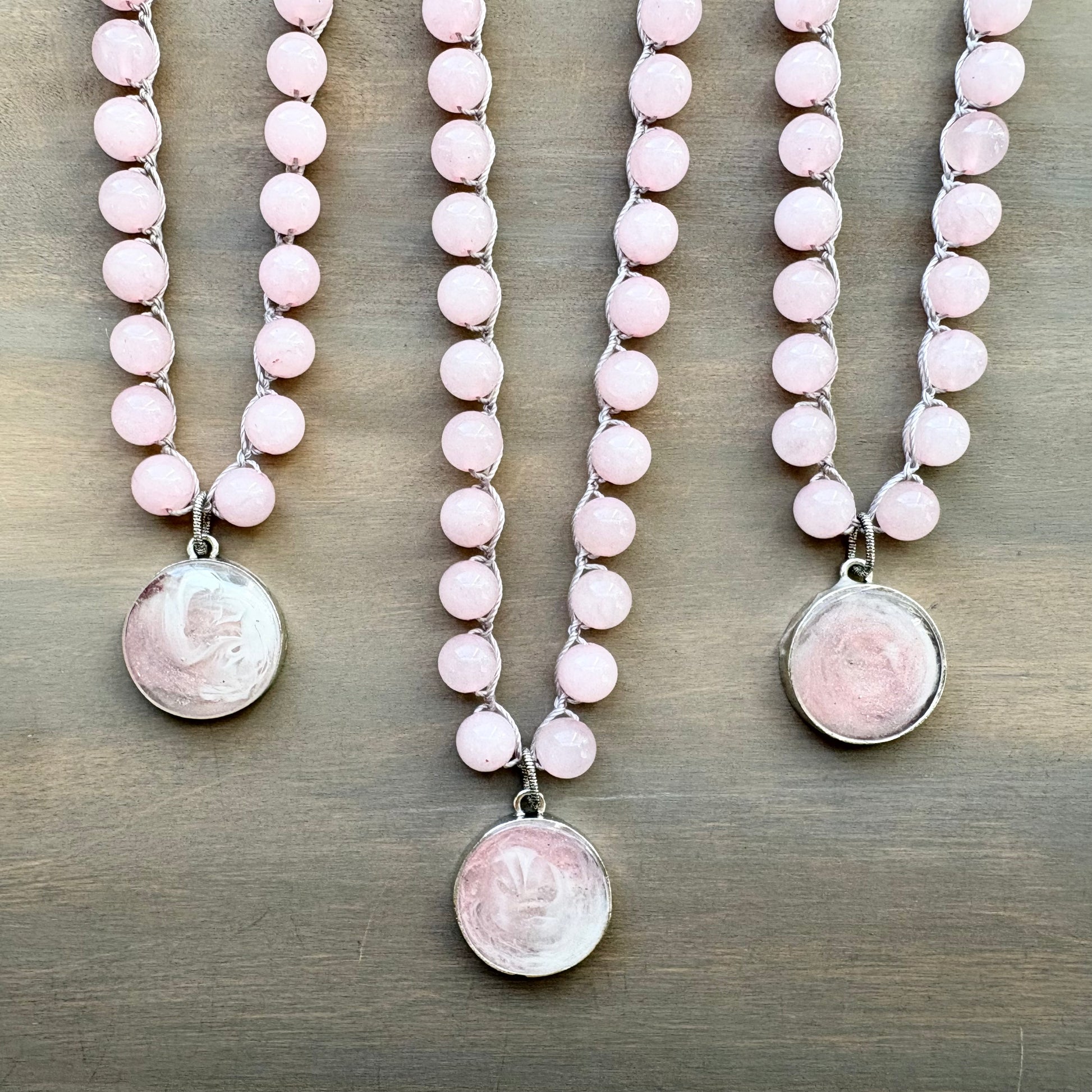 Three pink beaded necklaces with silver pendants on a wooden surface
