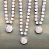 Three pink beaded necklaces with silver pendants on a wooden surface