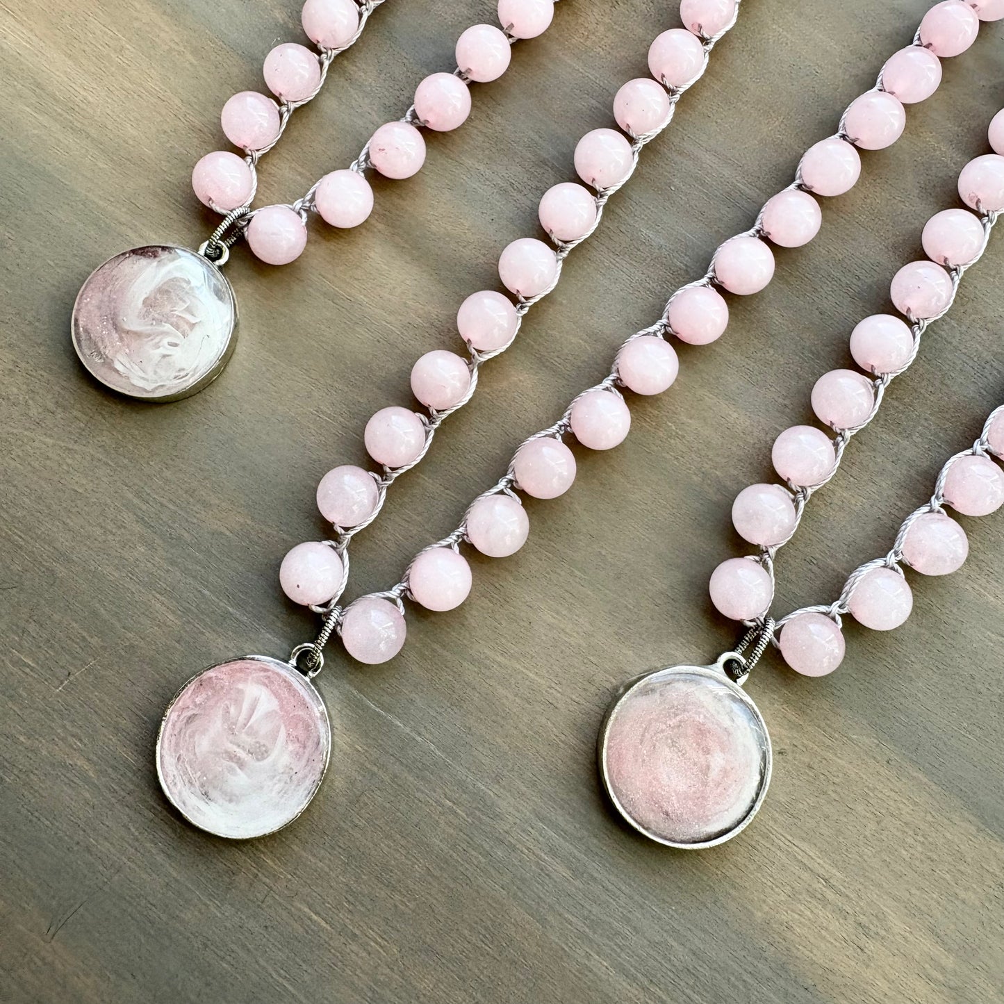 Two pink beaded necklaces with silver pendants on a wooden surface