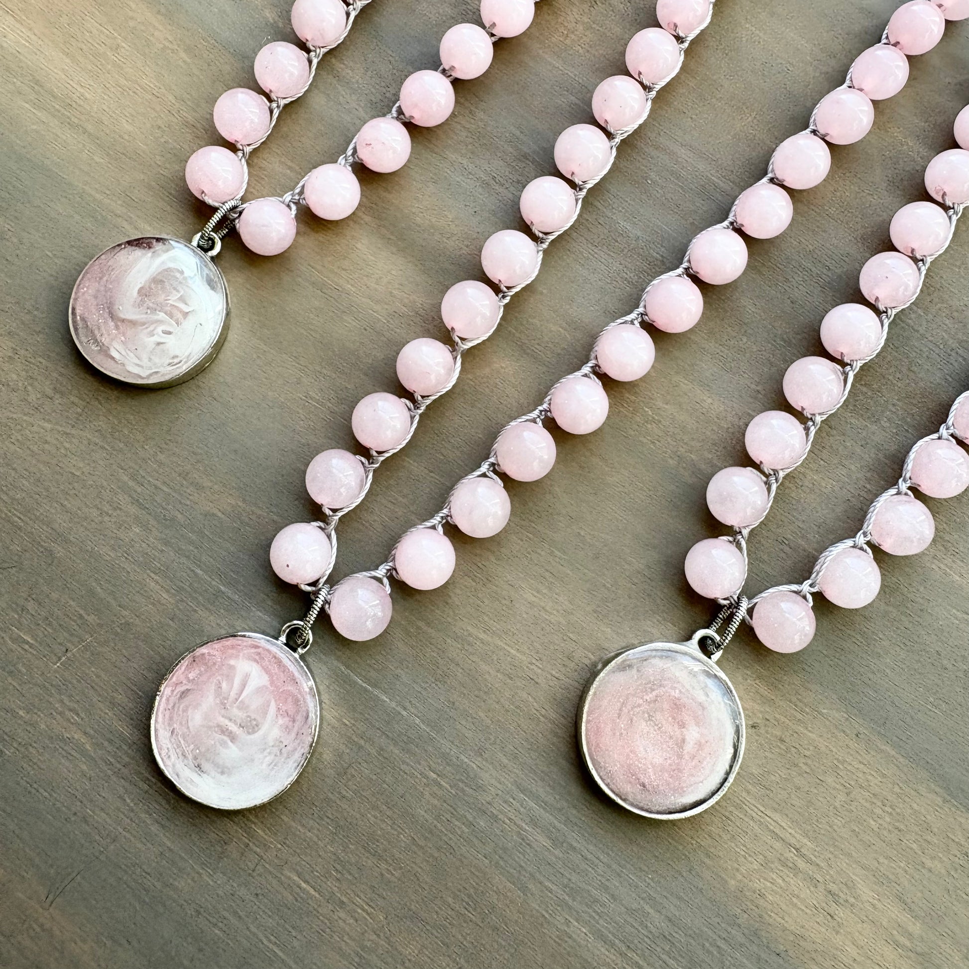 Two pink beaded necklaces with silver pendants on a wooden surface