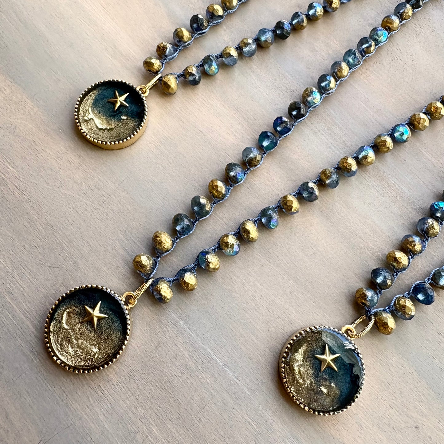Three beaded necklaces with celestial pendants on a wooden surface