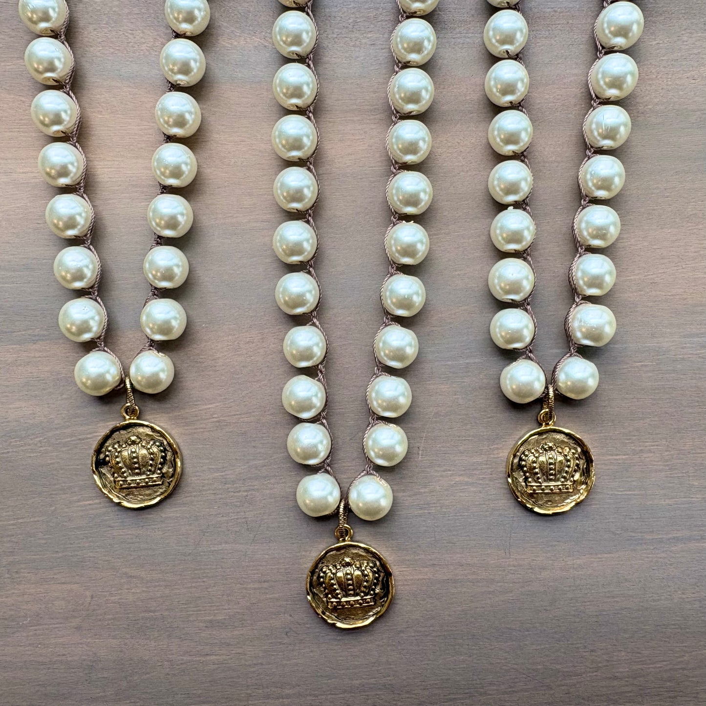 Three pearl necklaces with gold pendants on a wooden surface
