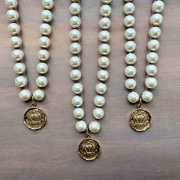 Three pearl necklaces with gold pendants on a wooden surface