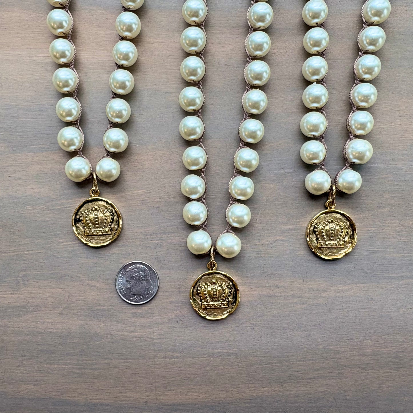 Three pearl necklaces with gold pendants on a wooden surface, one with a coin for size comparison.