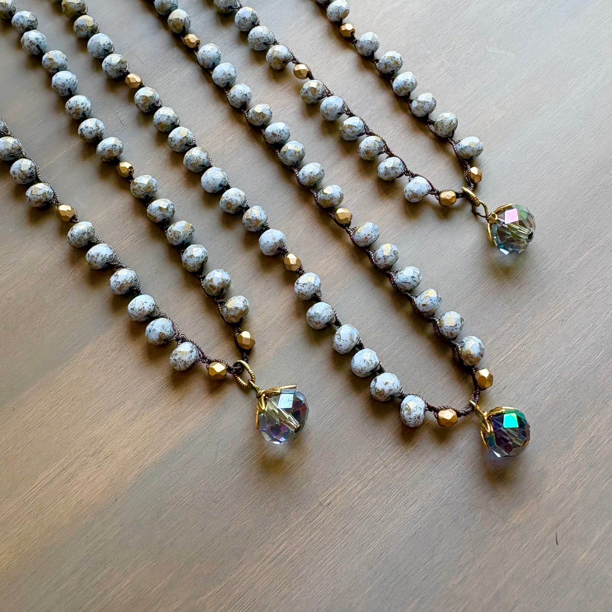 Three pearl necklaces with crystal pendants on a wooden surface