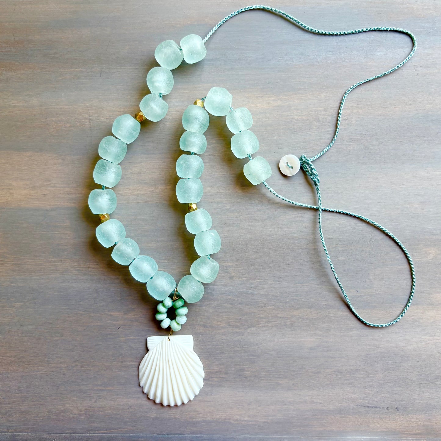 Necklace with light blue beads and a shell pendant on a wooden surface