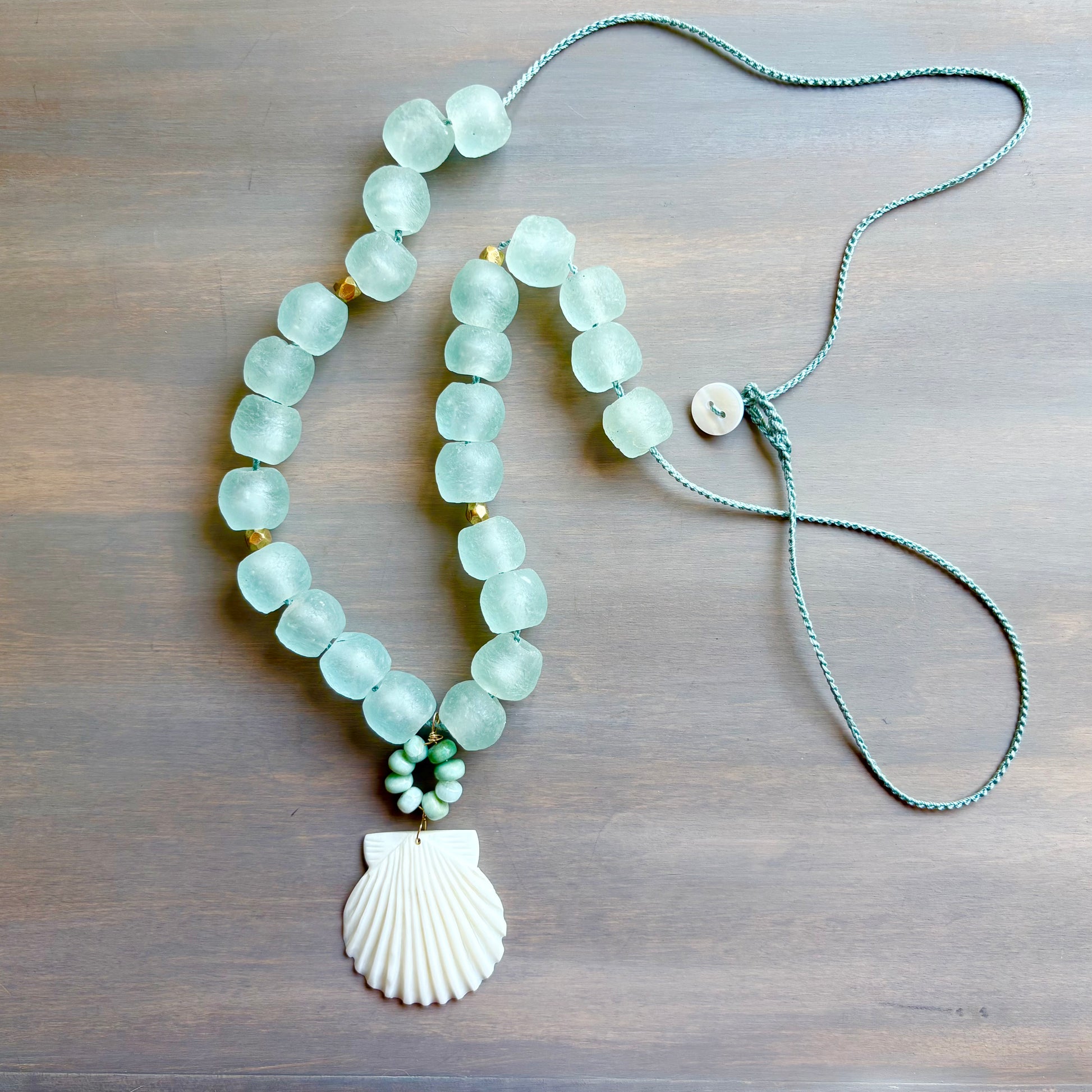 Necklace with light blue beads and a shell pendant on a wooden surface