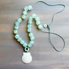 Necklace with light blue beads and a shell pendant on a wooden surface