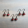 Set of red and black teardrop earrings on a metallic surface