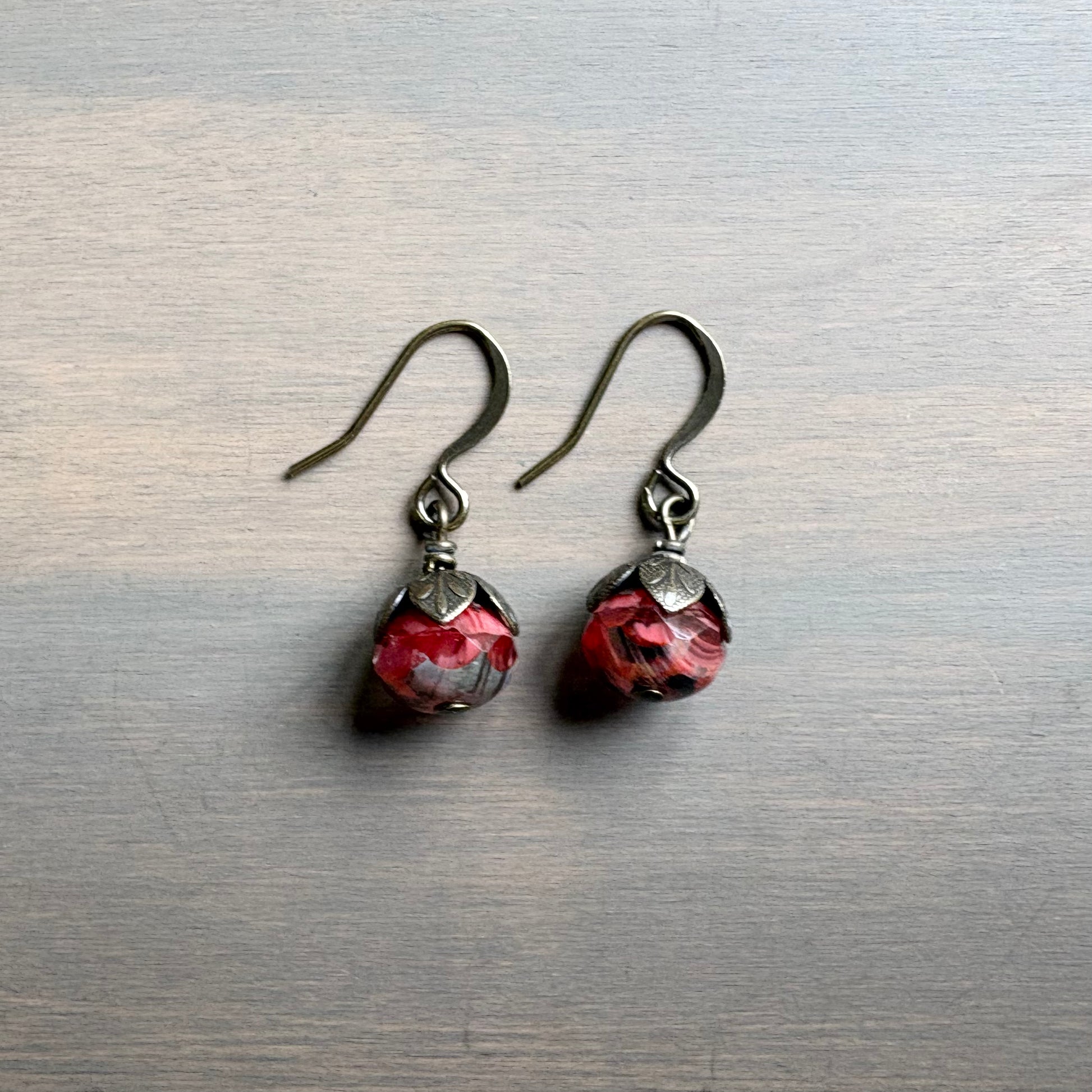 Pair of earrings with red and silver design on a metallic surface