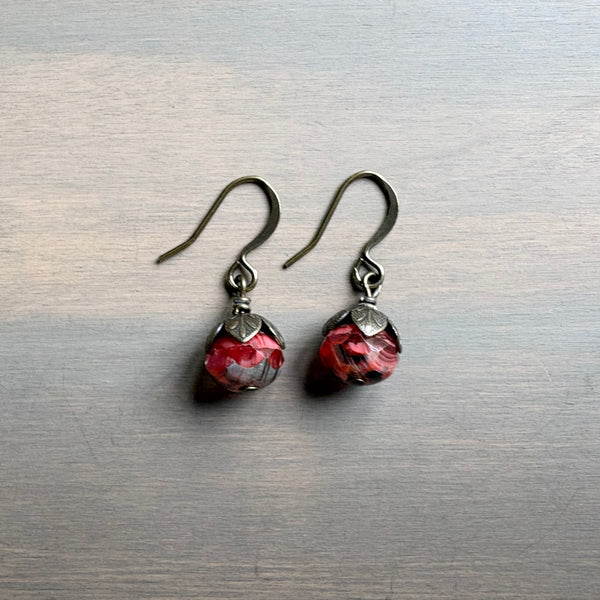 Pair of earrings with red and silver design on a metallic surface