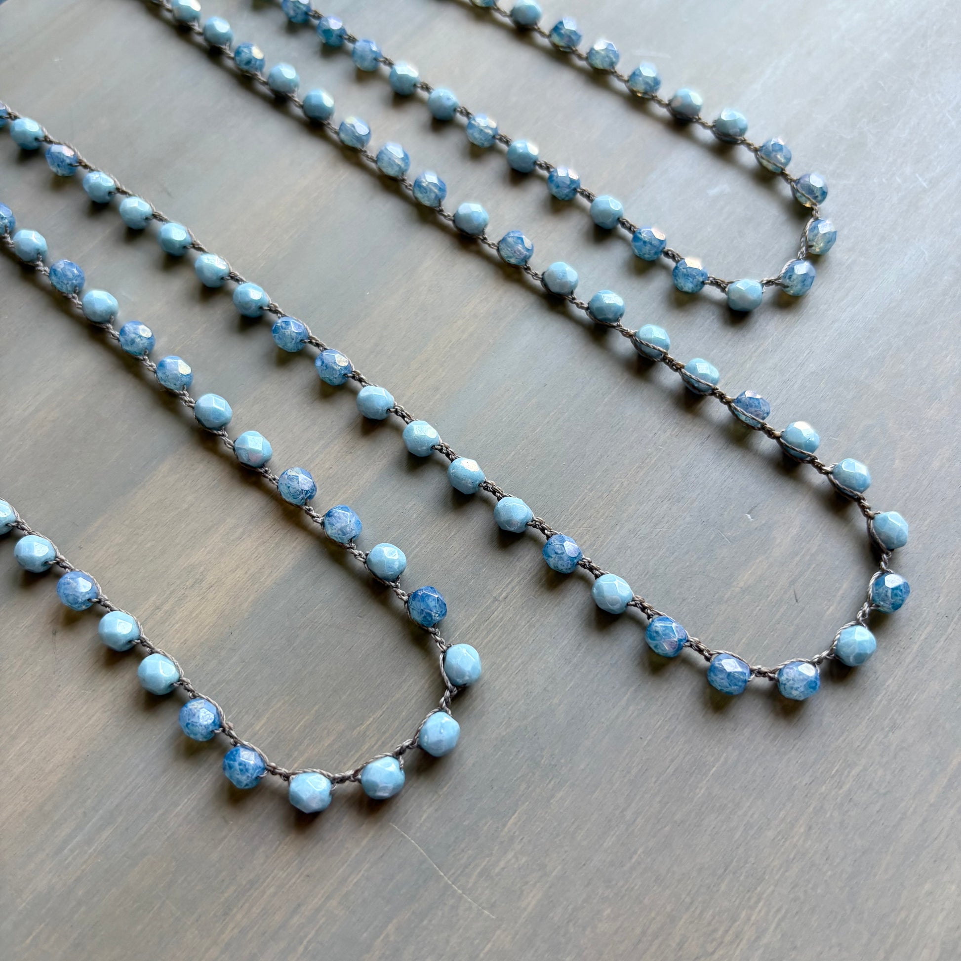 Two blue beaded necklaces on a wooden surface