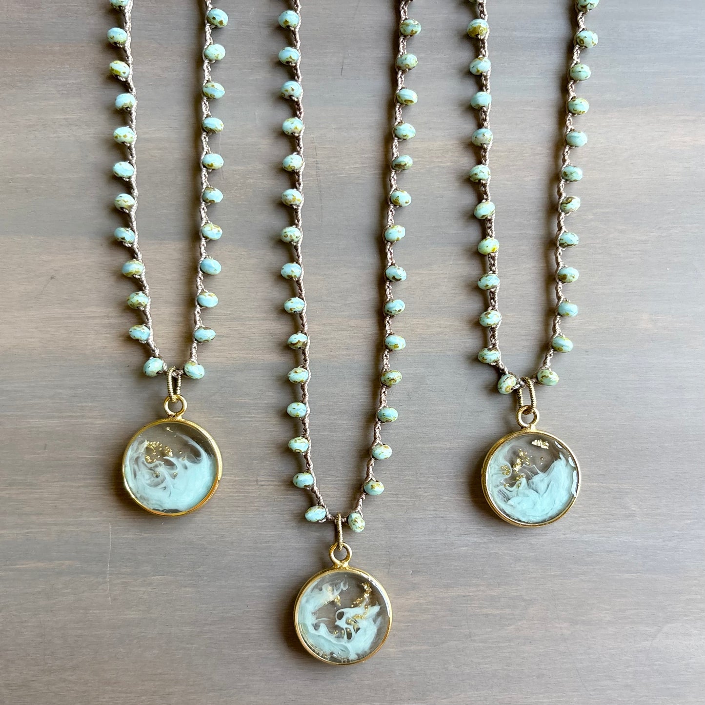 Three pearl necklaces with circular pendants on a wooden surface
