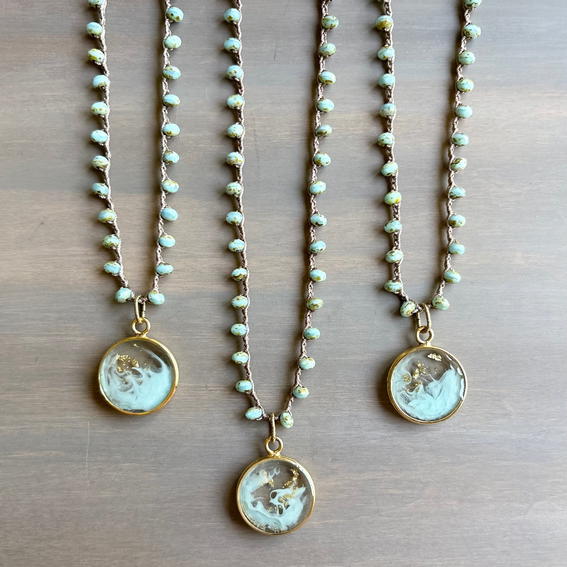 Three pearl necklaces with circular pendants on a wooden surface
