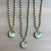 Three pearl necklaces with circular pendants on a wooden surface
