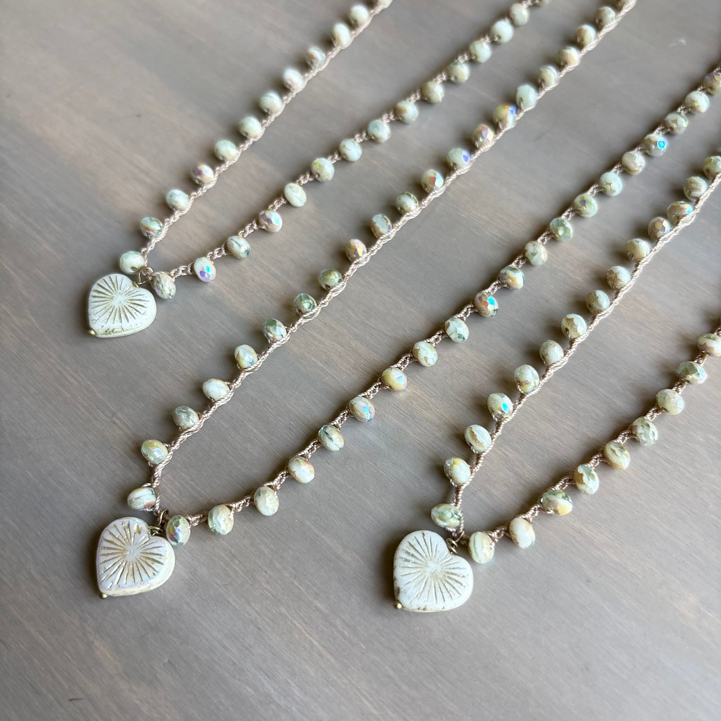 Three pearl necklaces with heart-shaped pendants on a wooden surface