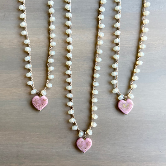 Three pearl necklaces with pink heart-shaped pendants on a wooden surface