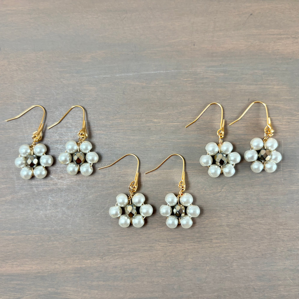 Four pairs of gold-tone dangle earrings with white pearl flower clusters, arranged on a gray wood-grain surface.