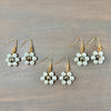 Four pairs of gold-tone dangle earrings with white pearl flower clusters, arranged on a gray wood-grain surface.