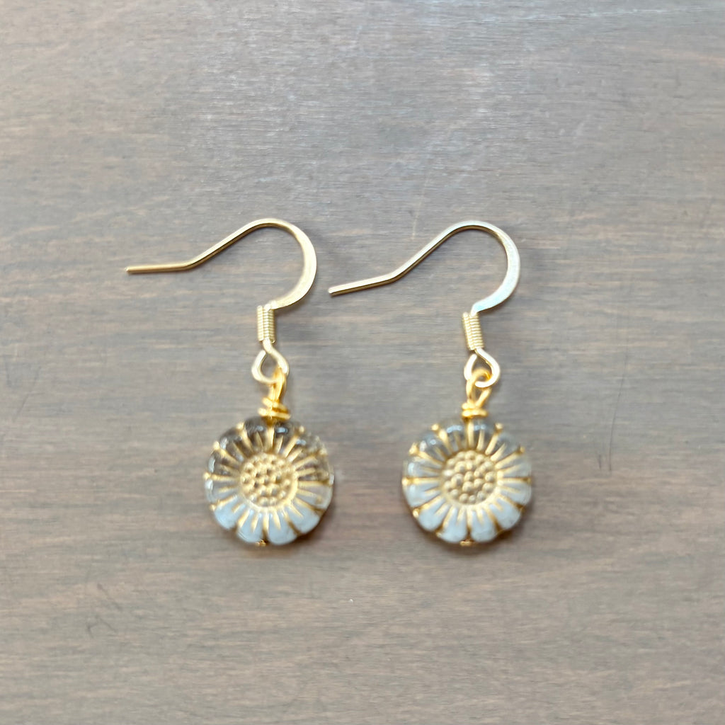 A pair of gold-tone daisy drop earrings with light blue enamel petals, displayed on a dark gray wooden surface.